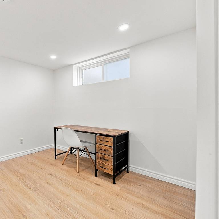 Finished basement used as a home office, with light wood flooring and a high basement window