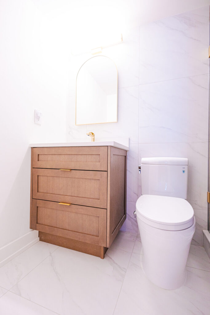 Wood-tone vanity with arched gold mirror and white marble walls