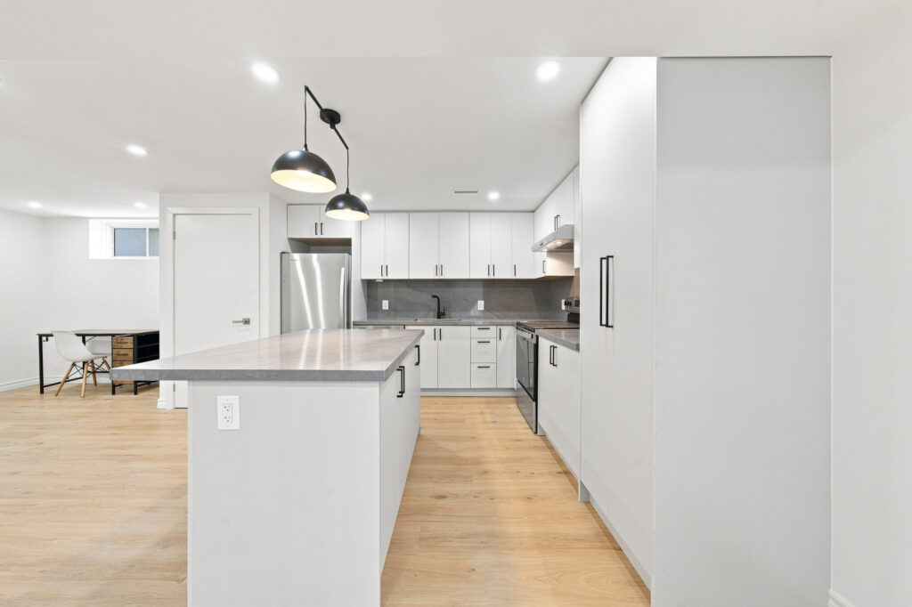Legal basement apartment kitchen with an island, white cabinets and black pendant lights